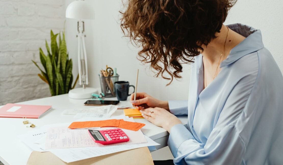 Une femme à son bureau calcule et écrit.