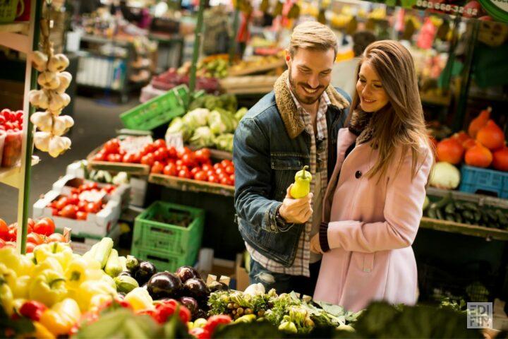 Un couple dans un marché à un stand de fruits et légumes.